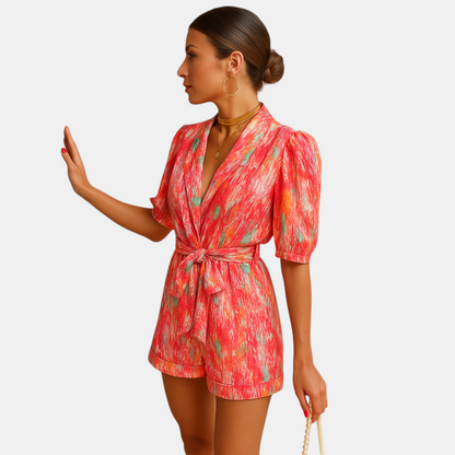 Dames zomerjumpsuit met levendige print, korte broek en taille-accentuerende riem, perfect voor warme dagen en casual gelegenheden.